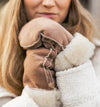 Close-up of a person wearing brown sheepskin mittens holding their hands together.