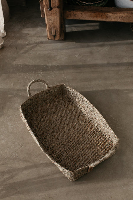 Shallow sea grass basket for storage or display placed on concrete floor