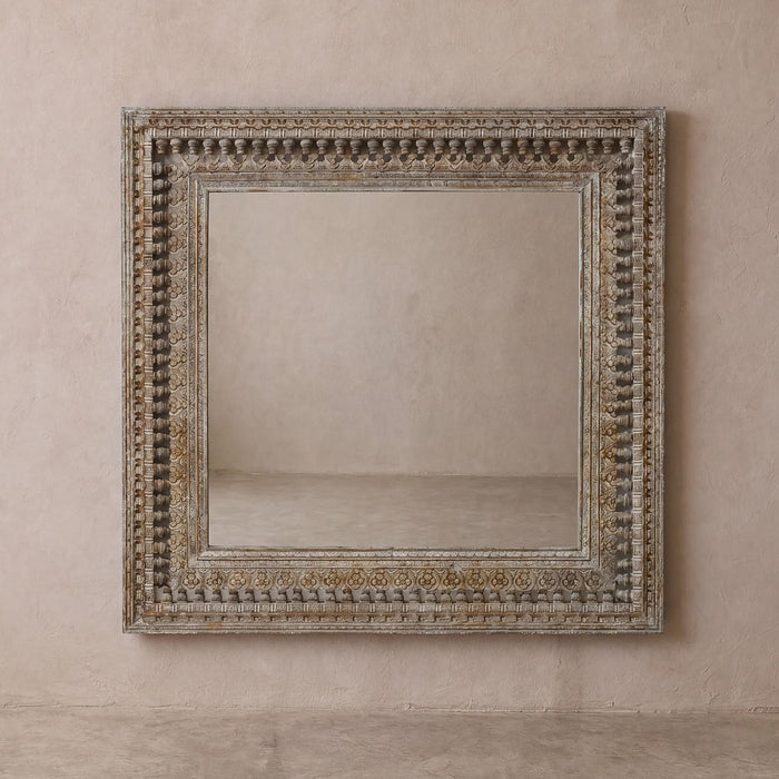 Distressed grey ornately carved teak mirror on a beige wall