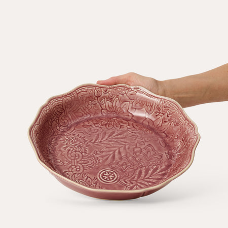 Rose coloured bowl with decorative glaze and hand in shot on white background