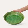 Green floral patterned ceramic pie dish on white background with hand in shot to show size