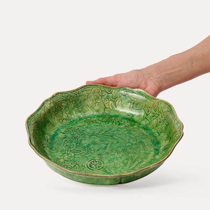 Green floral patterned ceramic pie dish on white background with hand in shot to show size