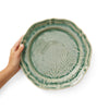Hand holding a green ceramic plate with leaf design on a white background