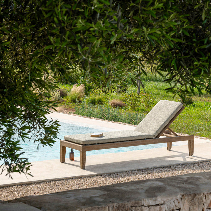 Chaise lounge by a pool with greenery in the background