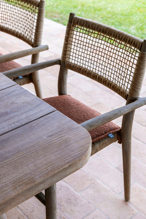 A close-up of a Gommaire Mieke Dining Chair with a rust cushion, showing the reclaimed teak wood frame and luxury rattan backrest and seat.