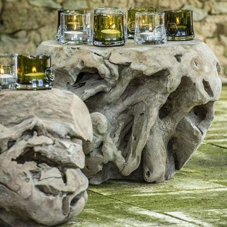 A teak root ball coffee table with multiple cups placed on top, set against a stone wall and paving