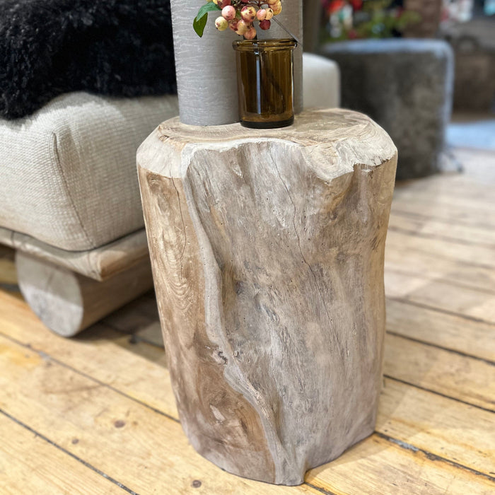 Section of teak root in a trunk shape with natural grooves and indentations on a wooden floor with candles and small glass with berries on top