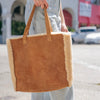 Brown tote bag with shearling lining held by a person on a blurred street background