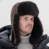 Man wearing a dark fur-trimmed winter hat and coat against a white background