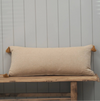 Golden yellow herringbone pattern bolster cushion with tassles on a wooden bench with painted grey wood background