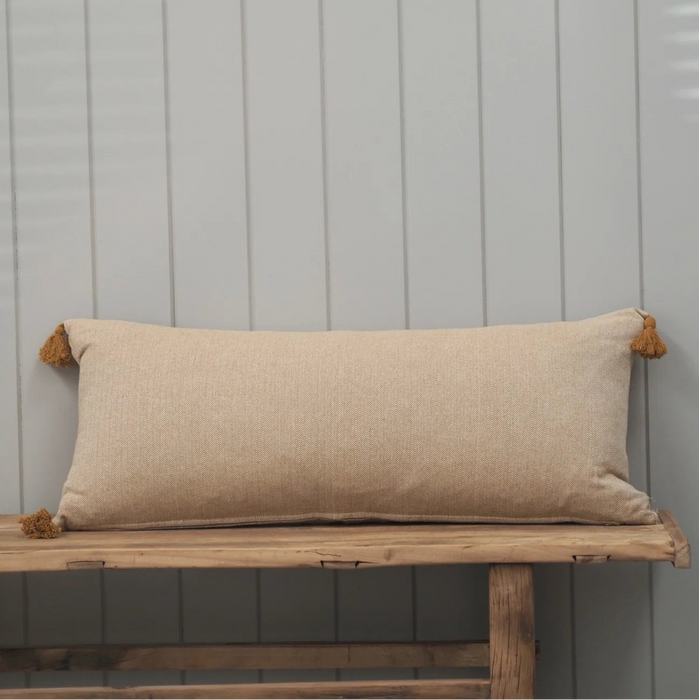Golden yellow herringbone pattern bolster cushion with tassles on a wooden bench with painted grey wood background